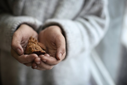 Poor woman holding piece of bread on blurred background