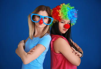Young women in funny disguise posing on color background. April fool's day celebration
