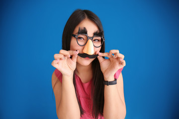 Young woman in funny disguise posing on color background. April fool's day celebration