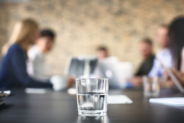 Glass of water and blurred office meeting on background. Finance trading