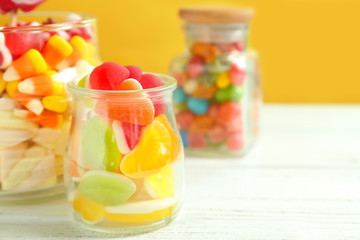 Glassware with different candies on table against color background