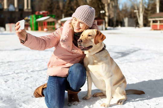 Woman taking selfie with cute dog outdoors on winter day