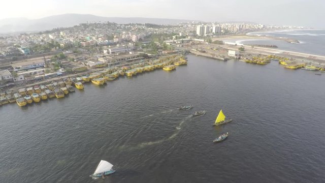 An aerial view of small yellow boats moored to the side of a pier, surrounding with ripples in the water.