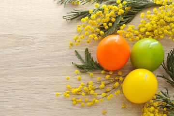 Religious international Easter holiday - candles in the form of colorful eggs, flowers (mimosa) and bright morning light. 
