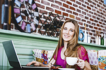 Beautiful young woman successful fashion and beautiful works on a laptop at the table with a Cup of coffee