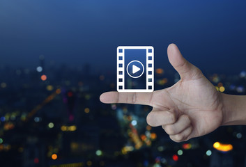 Play button with movie icon on finger over blur colorful night light city tower, Cinema online concept