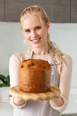 beautiful young woman holding easter cake on cutting board and smiling at camera