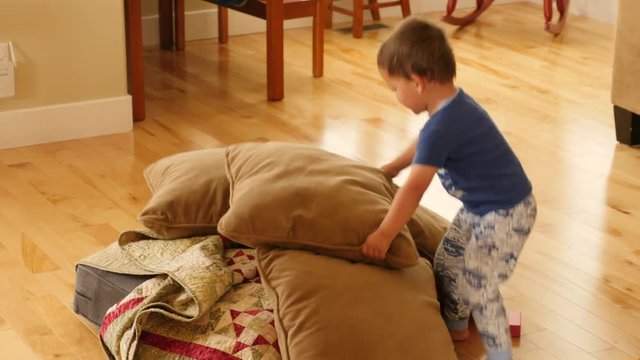 A boy builds a pillow and blanket fort on the ground