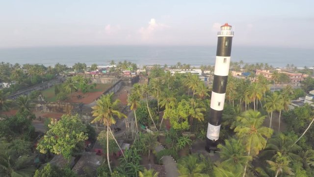 A stupendous view of a lighthouse surrounded by palm trees near a beach.