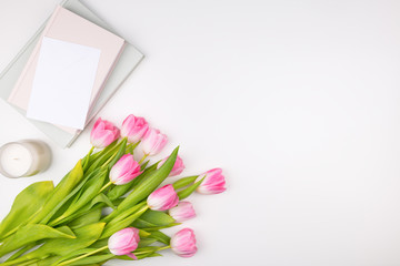 Minimal styled flat lay with pink tulips flowers with petals and white envelope, notebooks and candle. Mock up top view isolated on white. Feminine flat lay.
