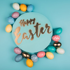 top view of round board with happy easter lettering and various colorful easter eggs on blue surface