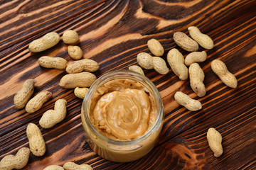 Bowl of peanut butter and peanuts on dark wooden background from top view. Space for text or design.