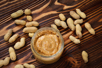 Bowl of peanut butter and peanuts on dark wooden background from top view. Space for text or design.