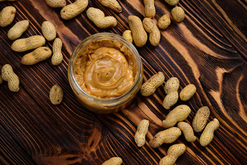 Bowl of peanut butter and peanuts on dark wooden background from top view. Space for text or design.