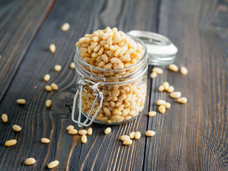 Side view of glass jar with a handful of pine nut, cedar nuts on a wooden background, selective...