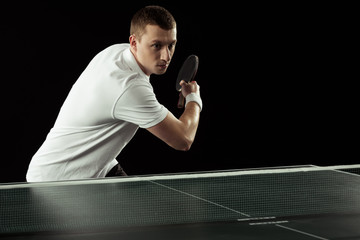 young focused tennis player in uniform practicing in table tennis isolated on black