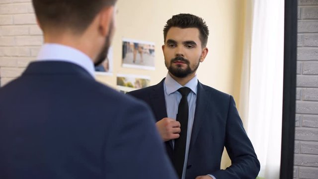 Young man in business suit getting ready for work interview in front of mirror