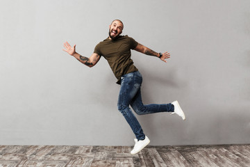 Fototapeta na wymiar Full-length image of smiling guy with tattoo on his arms having fun while posing on camera, isolated over gray background
