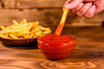 Hand with fresh french fry dipped into the tomato sauce