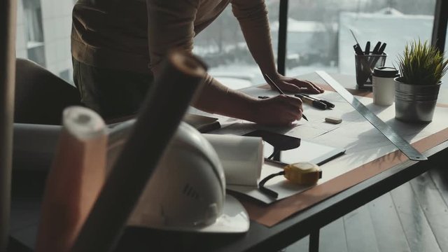 Architect's desk: drawings, tape measure, ruler and other drawing tools. Engineer works with drawings in a bright office, close-up. Insturments and office for designer. Male hands draw with a pencil.