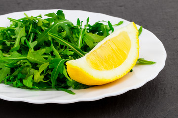 Fresh spring salad with rucola and lemon, in bowl on dark stone background with free text space
