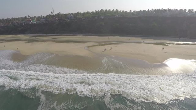 An aerial view of a gorgeous wave hitting the shore with beautiful tropical trees in the horizon.