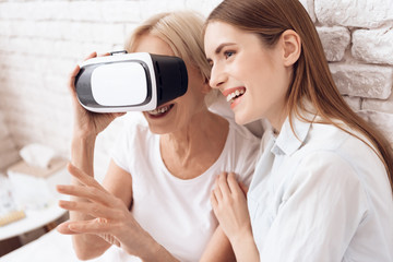 Girl is nursing elderly woman at home. They are using virtual reality.