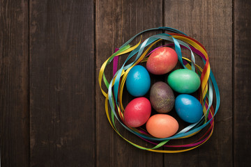 Easter eggs of different colors and bright ribbons on a wooden background.