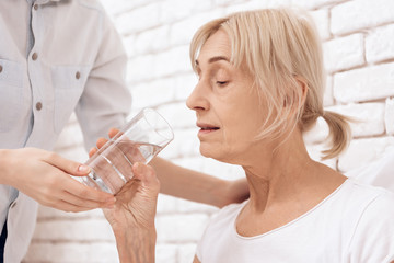 Girl is caring for elderly woman at home. Girl is helping woman with glass of water.