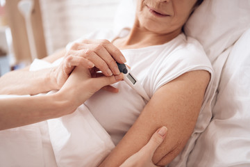 Girl is nursing elderly woman at home. Girl is checking temperature with electronic thermometer.