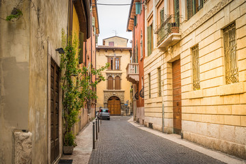 Fototapeta na wymiar Typical European small narrow cobblestone street with beautiful bright houses, windows with shutters. Bright sunny summer day in Italy, Verona