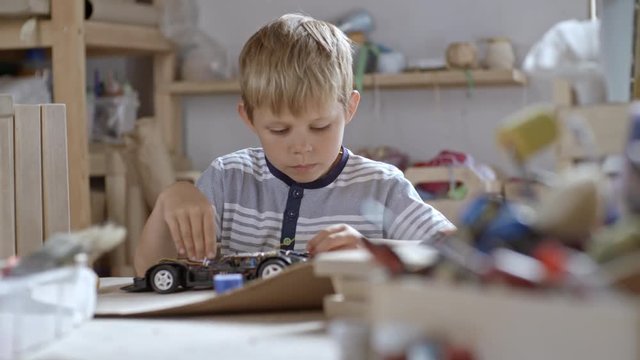 Medium shot of boy of primary school age trying to understand how cables work in his toy car in attempt to repair it