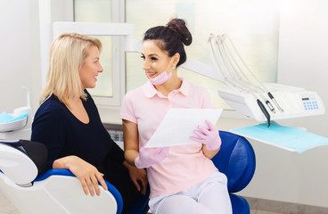 Fototapeta premium Young female doctor talking with woman patient and showing a radiograph x ray in stomatology clinic. Dentist concept.