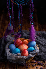 Unusually painted eggs in a wicker basket on a wooden background.