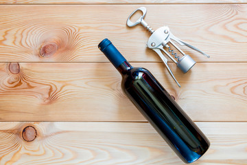 a bottle of red wine and a corkscrew on wooden boards top view close-up