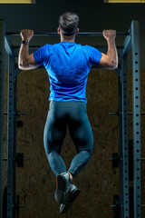 Fototapeta na wymiar the athlete pulls himself up on the bar in the gym view from the back