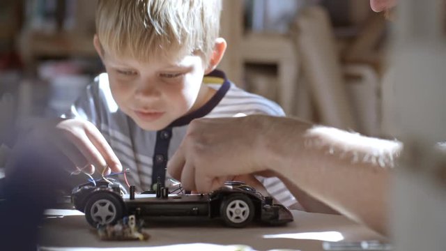 Boy of primary school age untying cables of deconstructed toy car when trying to fix it with help of his father