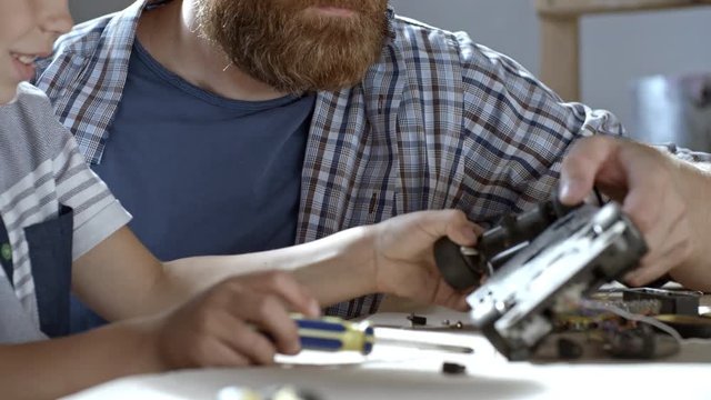 Boy of primary school age deconstructing his toy car and trying to fix it with help of his father