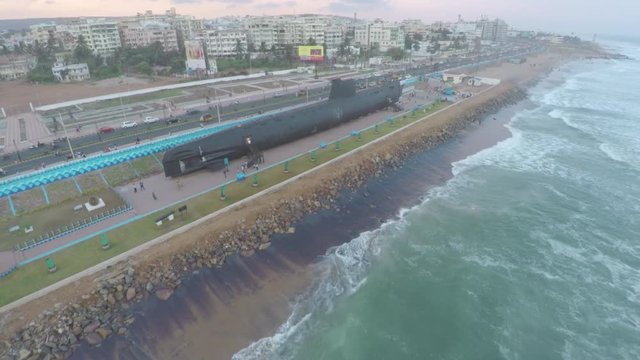 An aerial view of a submarine stationed by the beach for public display with waves crashing on the shore.