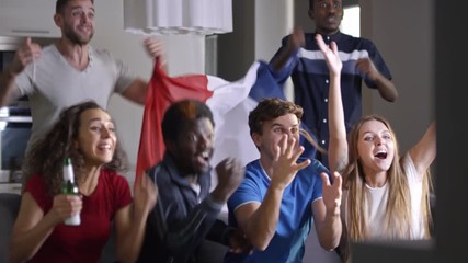 Mixed-raced company of excited men and women holding flag of France and watching match on TV at home. Friends yelling and embracing while celebrating winning of team