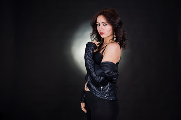 Studio portrait of sexy brunette girl in black leather jacket against black background.