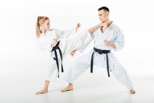 Female karate fighter kicking male partner isolated on white