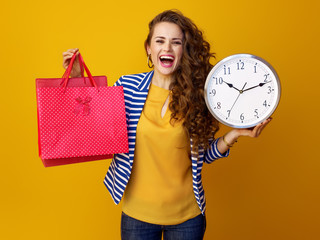 woman on yellow background showing clock and red shopping bags