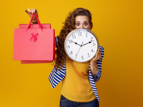 Surprised Woman Hiding Behind Clock And Showing Shopping Bags