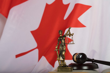 Statue of Themis and judge's gavel on a book. Flag of Canada in the background.