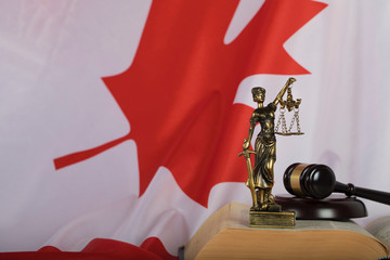 Statue of Themis and judge's gavel on a book. Flag of Canada in the background.