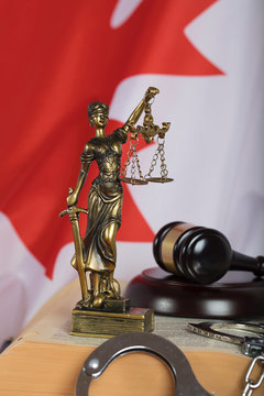 Statue of Themis and judge's gavel on a book. Flag of Canada in the background.