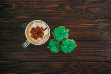 top view of cappuccino and cookies in shape of shamrocks on wooden table