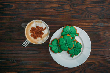 top view of tasty cappuccino and cookies in shape of clovers on wooden table