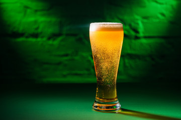 close-up view of glass with fresh cold amber beer in green light, saint patricks day concept